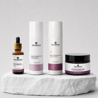 Four Dermaximíé skincare products arranged on a white stone slab against a light gray studio background: a brown dropper bottle, two tall white tubes, and a black-lidded jar. The products feature white labels with purple accents and black branding.