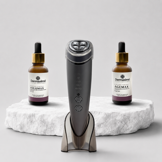A Dermaximío facial device stands upright on a clear stand in the center, flanked by two amber dropper bottles on a white stone slab against a light gray studio background.